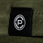 Close-up of a black fabric patch with a white circular 'CP' logo, sewn onto an olive green ribbed textile surface.