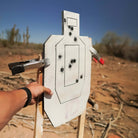 Target with bullet holes held by a person in an outdoor setting