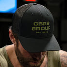 Person wearing the GBRS Group Instructor Trucker Hat – Anniversary Edition while training indoors, showcasing the structured fit and thermal graphic front logo