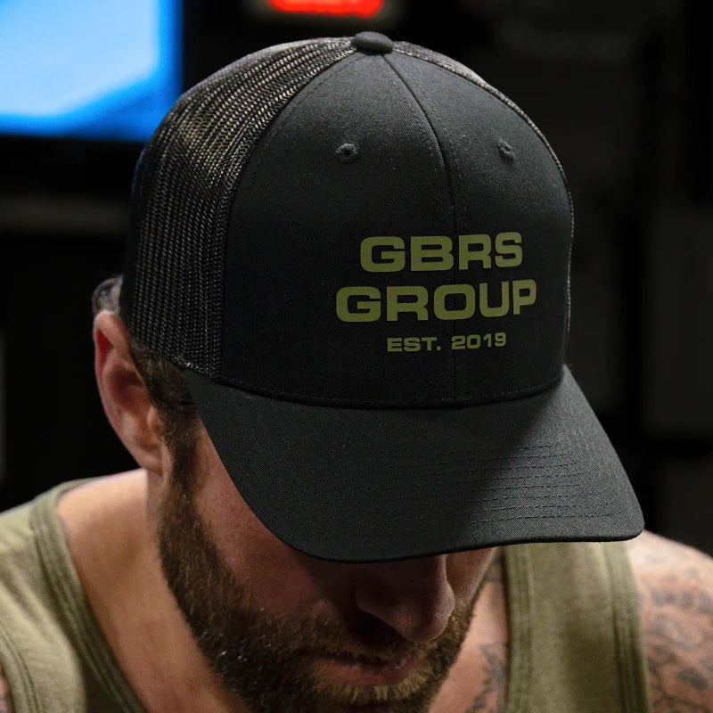 Person wearing the GBRS Group Instructor Trucker Hat – Anniversary Edition while training indoors, showcasing the structured fit and thermal graphic front logo