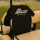 Black t-shirt with 'illicit' text logo on a golf cart seat