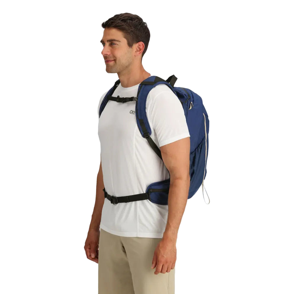 Three-quarter lifestyle view of the Outdoor Research Adrenaline Day Pack 30L in Cenote navy blue, showing ergonomic shoulder straps and padded waist strap for secure, balanced alpine and hiking carry.