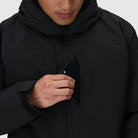 Close-up of the Outdoor Research Allies Colossus II Parka showing a phone being placed into the front chest pocket, highlighting secure waterproof storage designed for tactical gear, survival essentials, and cold-weather operations in Arctic conditions.
