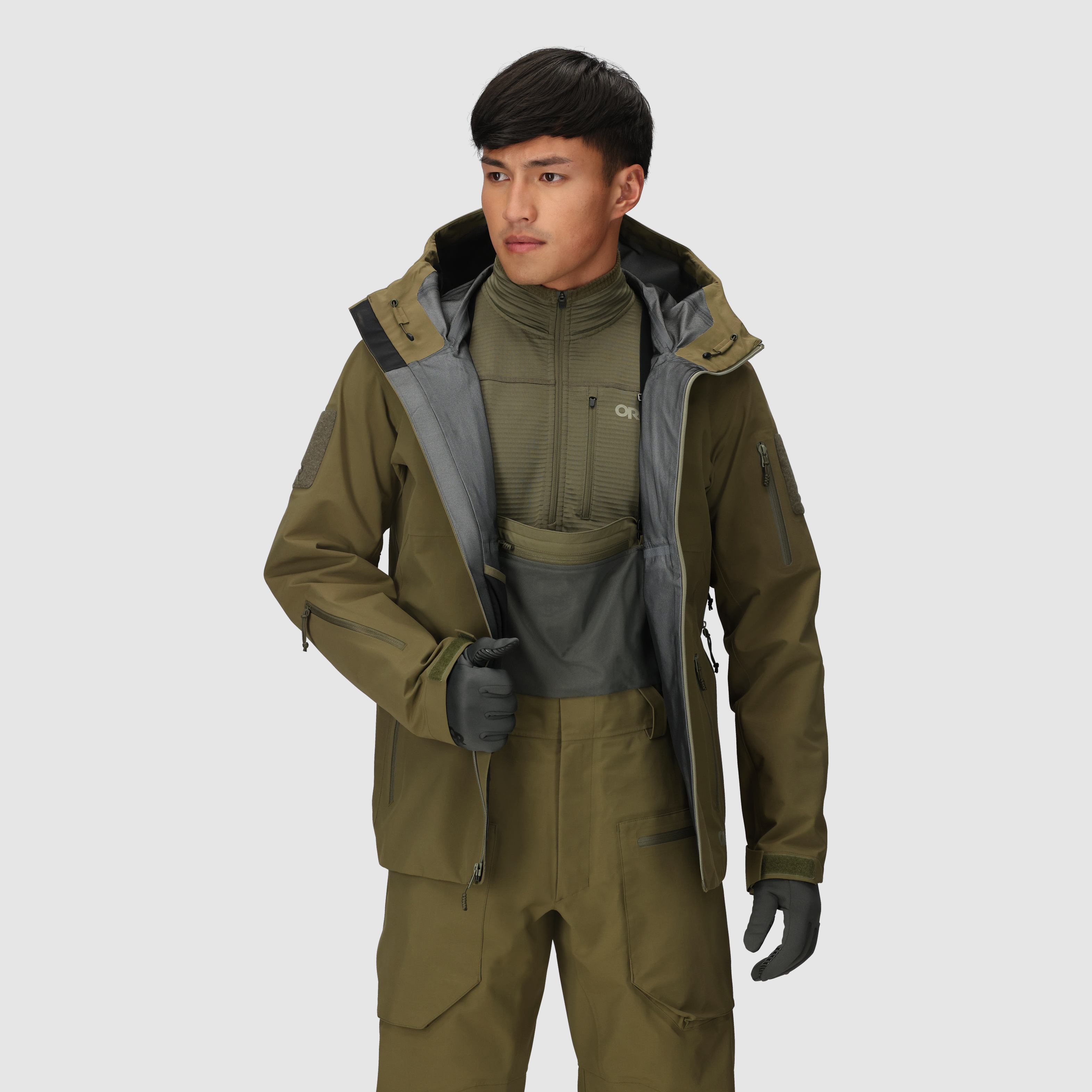 On-body view of the Outdoor Research Allies Mountain II Jacket in Ranger Green worn open, showing the AscentShell waterproof tactical construction, Cordura ripstop durability, articulated combat fit, and mission-ready design for military, law enforcement, and alpine professionals needing rugged weather protection with full mobility.