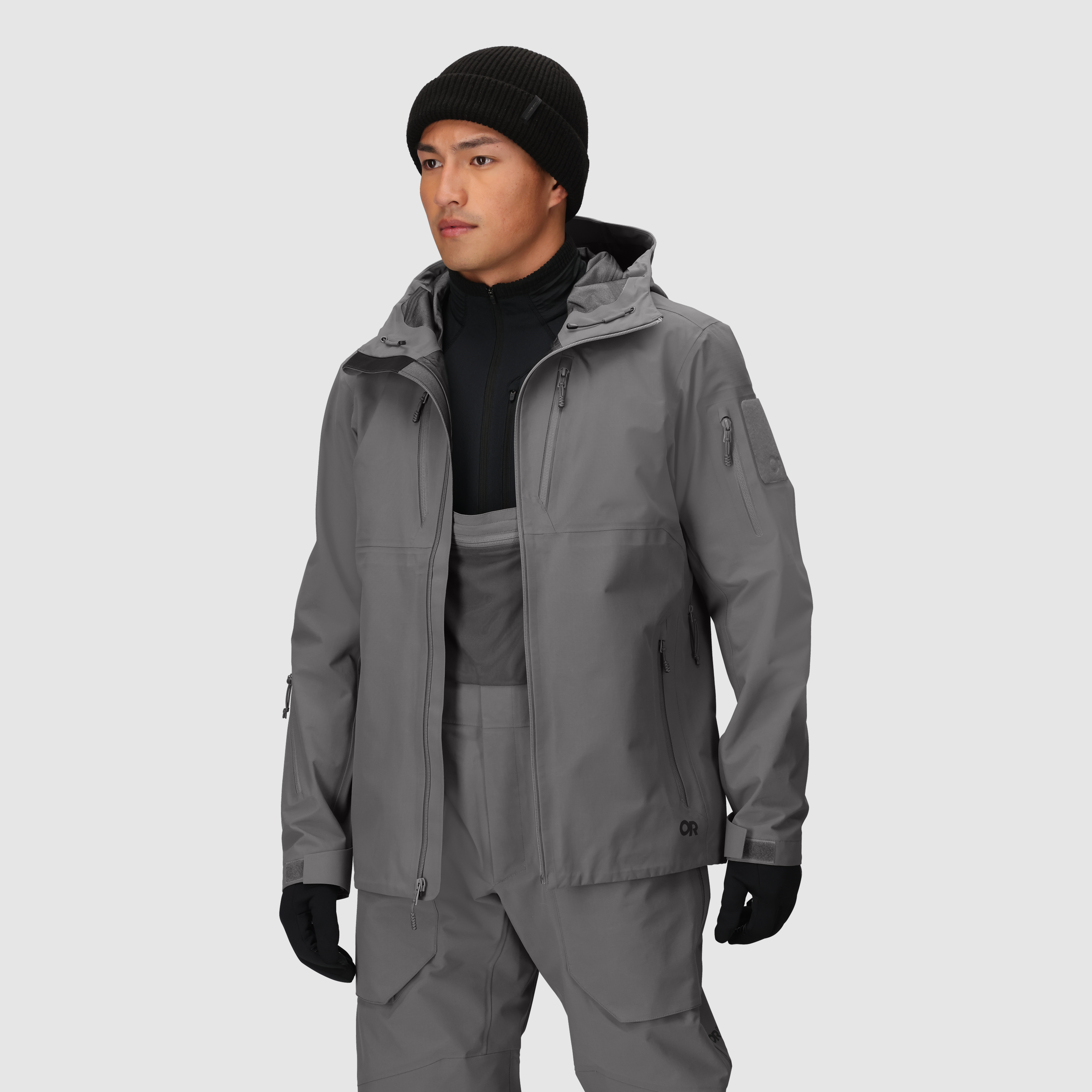 On-body view of the Outdoor Research Allies Mountain II Jacket in Wolf Grey worn unzipped, showing the AscentShell waterproof tactical construction, Cordura ripstop durability, articulated combat fit, and mission-ready design for military, law enforcement, and alpine professionals operating in extreme weather.