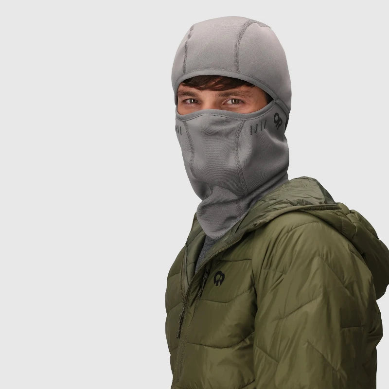 Person wearing a gray balaclava and green jacket on a light gray background