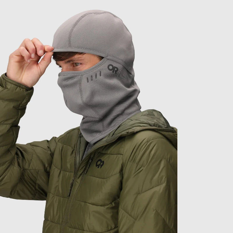 Person wearing a gray balaclava and green jacket with a brand logo on a light gray background