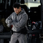 Lifestyle image of the Outdoor Research Shadow Hybrid Hoodie worn as part of a full tactical kit, showing hybrid insulated front, breathable stretch back panels, and low-profile hood designed for military operations, alpine climbing, and active cold-weather missions.