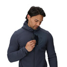 Detail view of the Outdoor Research Vigor Plus Fleece Hoodie showing a man placing a phone into the zippered chest pocket, highlighting secure storage and easy access for essentials during cold-weather pursuits.