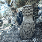 On body view of the Salomon FORCES Quest 4D 2 High GTX boots worn while kneeling in military uniform showing the waterproof GORE TEX construction, high cut support, and 4D Advanced Chassis stability built for rugged terrain, extended rucking, and tactical field operations.