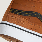 Close-up of a brown suede boot with white sole and black stitching on a light gray background