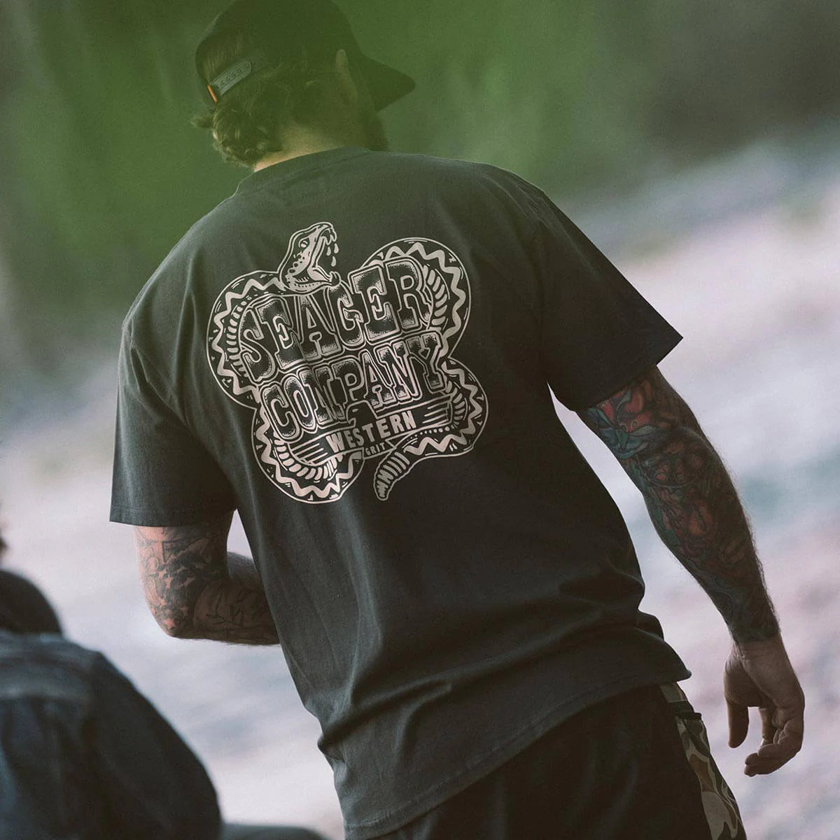 Lifestyle image of the Seager Rattler Tee in Vintage Black, showing the bold coiled rattlesnake back graphic, a western heritage print on premium cotton built for rugged everyday wear.