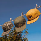 TD Goat Rope Snapback Caps in Mossy Oak OG Bottomland, Biscuit, and Loden worn outdoors on a sunny day, highlighting the lightweight five-panel design, rope detail, and breathable construction for warm-weather everyday wear.