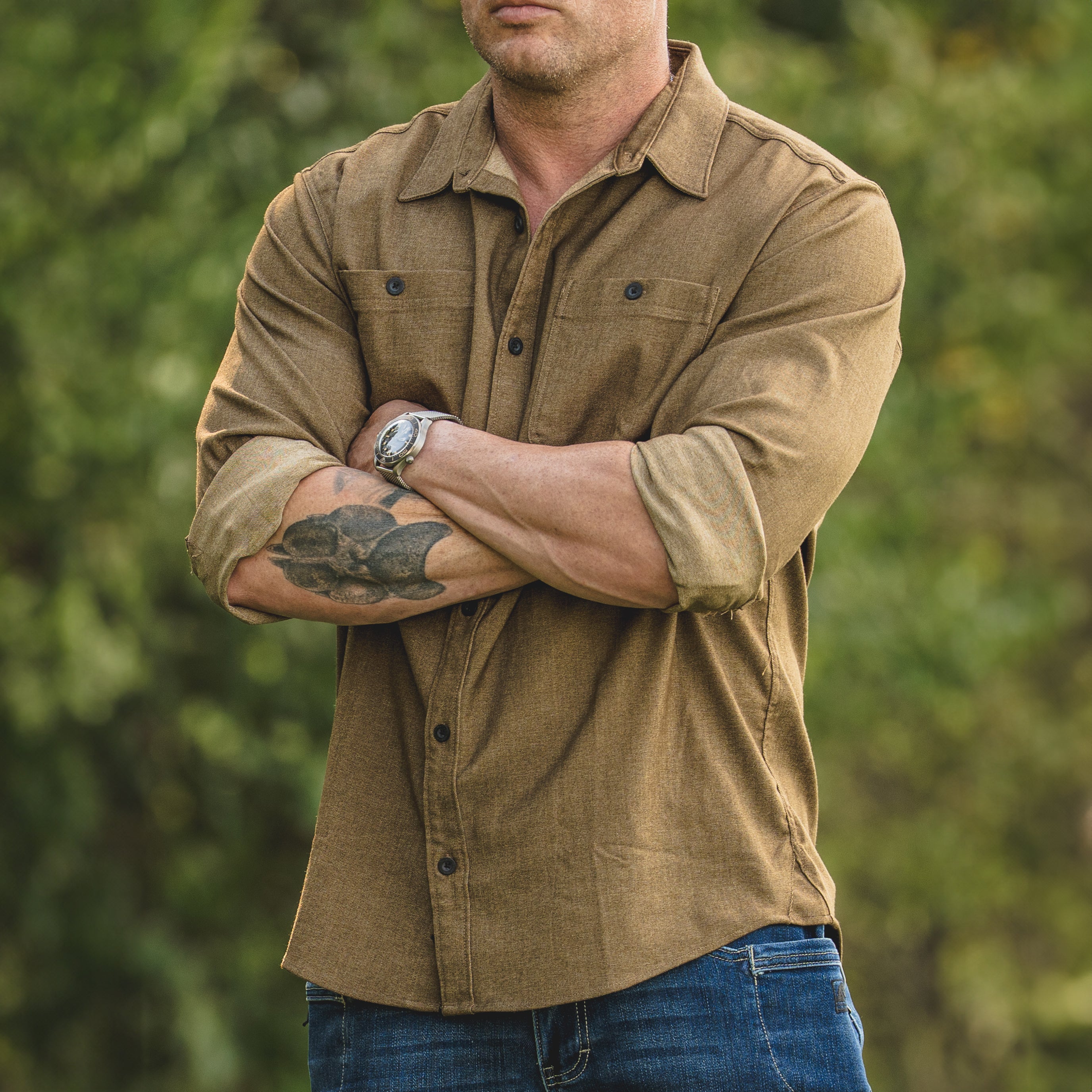 Lifestyle photo of a man outdoors wearing the brass TD Stretch Flannel Work Shirt with TD McQuade V2 Jeans, a soft and comfortable tactical flannel built for Range Day and rugged workwear style.