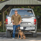 Outdoor lifestyle photo of a man with his truck and dog wearing the brass TD Stretch Flannel Work Shirt, a durable tactical flannel delivering rugged comfort for range days, camping, and everyday wear.