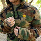 Close-up detail of the TD x Black Rifle Coffee Co. Reticle Half-Zip Fleece highlighting the woodland camo Sherpa fleece texture, half-zip front, and co-branded TD x BRCC logo patch. Durable birdseye mesh trim adds structure and breathability to this premium tactical fleece built for warmth, comfort, and all-day performance.