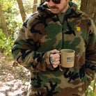 Man wearing the TD x Black Rifle Coffee Co. Reticle Half-Zip Fleece in woodland camo, showing relaxed fit and high-pile Sherpa fleece warmth. Tactical pullover built for cold-weather comfort with breathable mesh trim and co-branded TD x BRCC detailing. Perfect for range days, coffee runs, and off-duty missions.