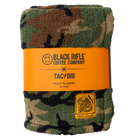 TD x Black Rifle Coffee Co. Woodland Throw Blanket shown folded inside branded sleeve packaging. Features dual-sided woodland camo fleece, co-branded TD x BRCC patch label, and high-loft polyester for ultimate warmth and comfort. Perfect tactical gift or off-duty essential for Black Rifle Coffee fans and outdoor adventurers.