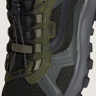 Close-up of a green and black hiking boot with brand logo on a beige background