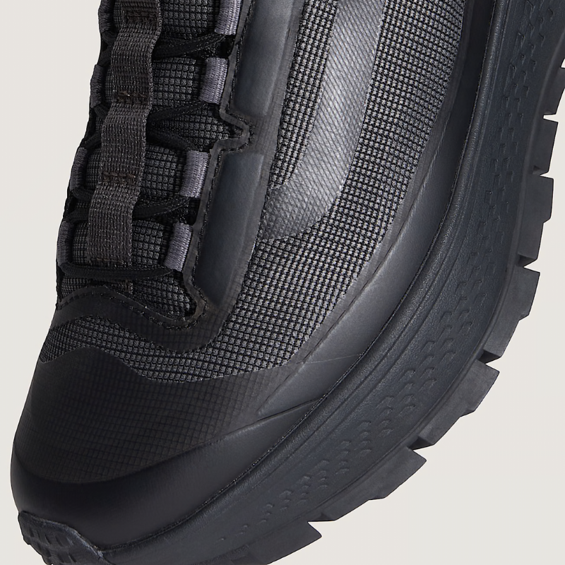 Close-up of a black hiking boot with mesh side panel on a beige background
