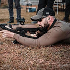 Lifestyle image of the Velocity Systems BOSS Rugby Long Sleeve Combat Shirt worn during prone shooting at the range, highlighting its athletic fit, breathable 4-way stretch nylon-spandex fabric, and moisture-wicking performance. Designed for military and law enforcement operators, this long sleeve tactical range shirt offers durability, mobility, and comfort while shooting from the ground or behind cover. Built in the USA with Odorexx™ antimicrobial control, UV protection, and sleeve pockets for field use.