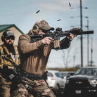 Lifestyle image of the Velocity Systems BOSS Rugby Long Sleeve Combat Shirt worn while shooting, highlighting its athletic fit, breathable 4-way stretch nylon-spandex fabric, and sling-friendly low-profile collar. Built for tactical shooters, law enforcement, and military operators, this combat base layer provides unrestricted movement, moisture-wicking comfort, and durable performance during firearms training, live range drills, and dynamic shooting scenarios. Made in the USA and available at Tac Dis.