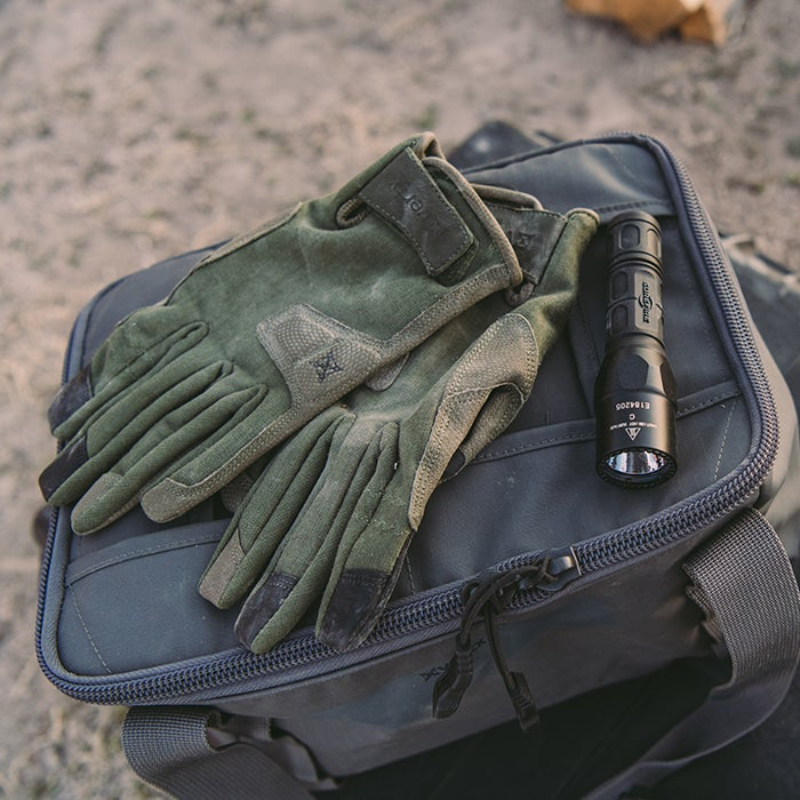 Ranger green Vertx tactical gloves and flashlight on a black bag outdoors