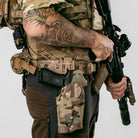 Person fully kitted out in tactical gear holding a rifle on a plain background