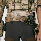 Person wearing camouflage military uniform with tactical gear on a plain background