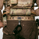 Person wearing a tactical vest with camouflage pattern and carrying equipment.