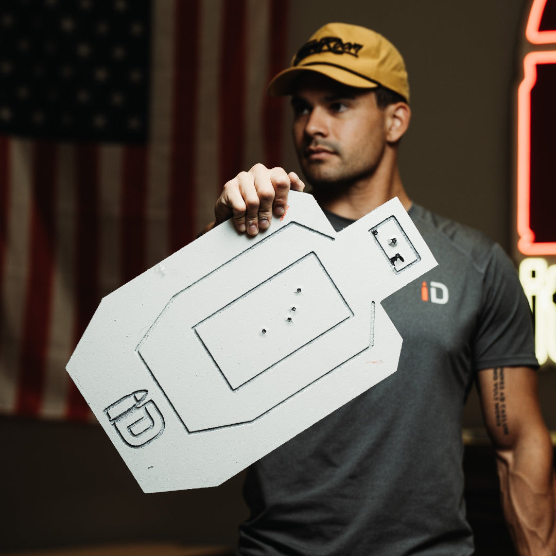 Man holding a white range target in front of an American flag and neon sign.