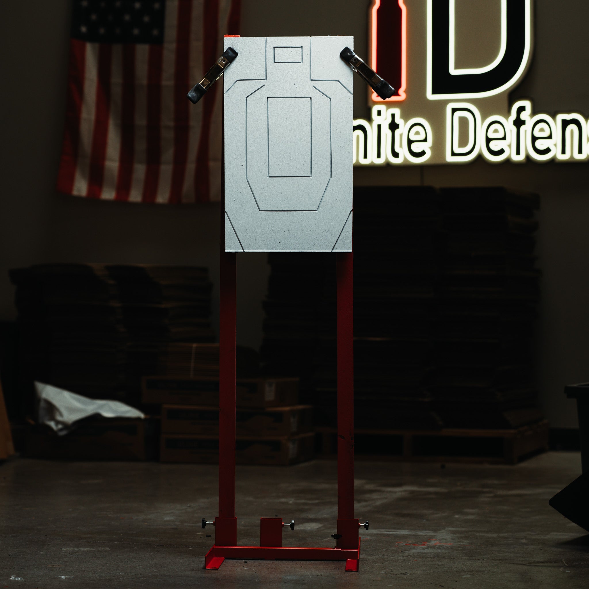Target practice stand with a target on a stand in a room with an American flag and 'Infinite Defense' sign.