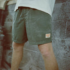 Person wearing green shorts with a brand logo against a stone wall.