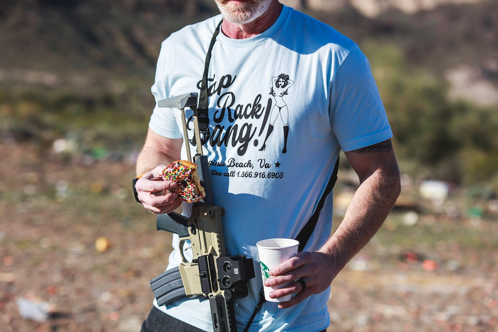 man wearing TD Tap Rack Bang Tee, holding coffee and donut in open field